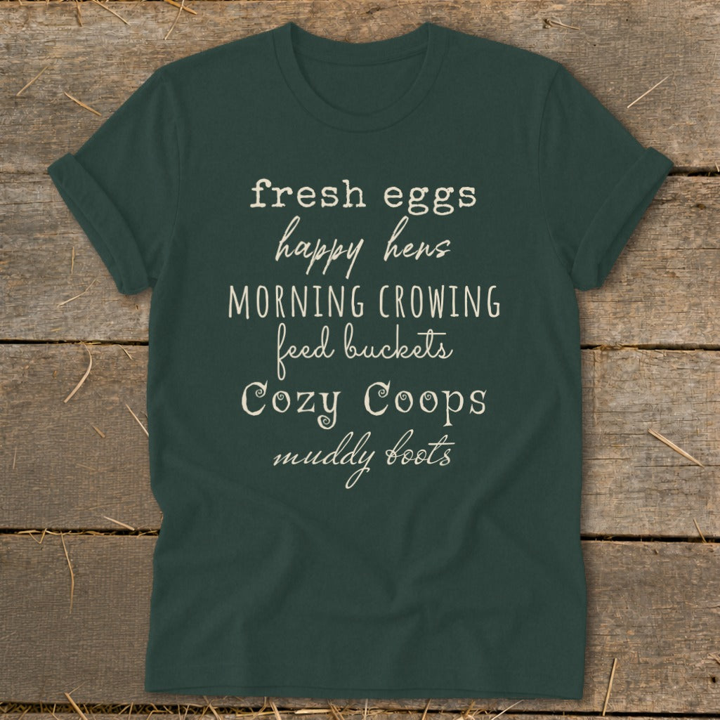 Dark green t-shirt with white text listing "fresh eggs happy hens MORNING CROWING feed buckets Cozy Coops muddy boots".