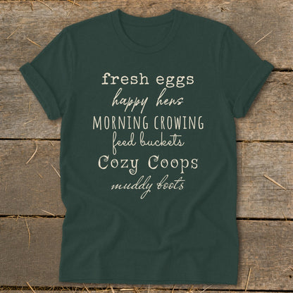 Dark green t-shirt with white text listing "fresh eggs happy hens MORNING CROWING feed buckets Cozy Coops muddy boots".
