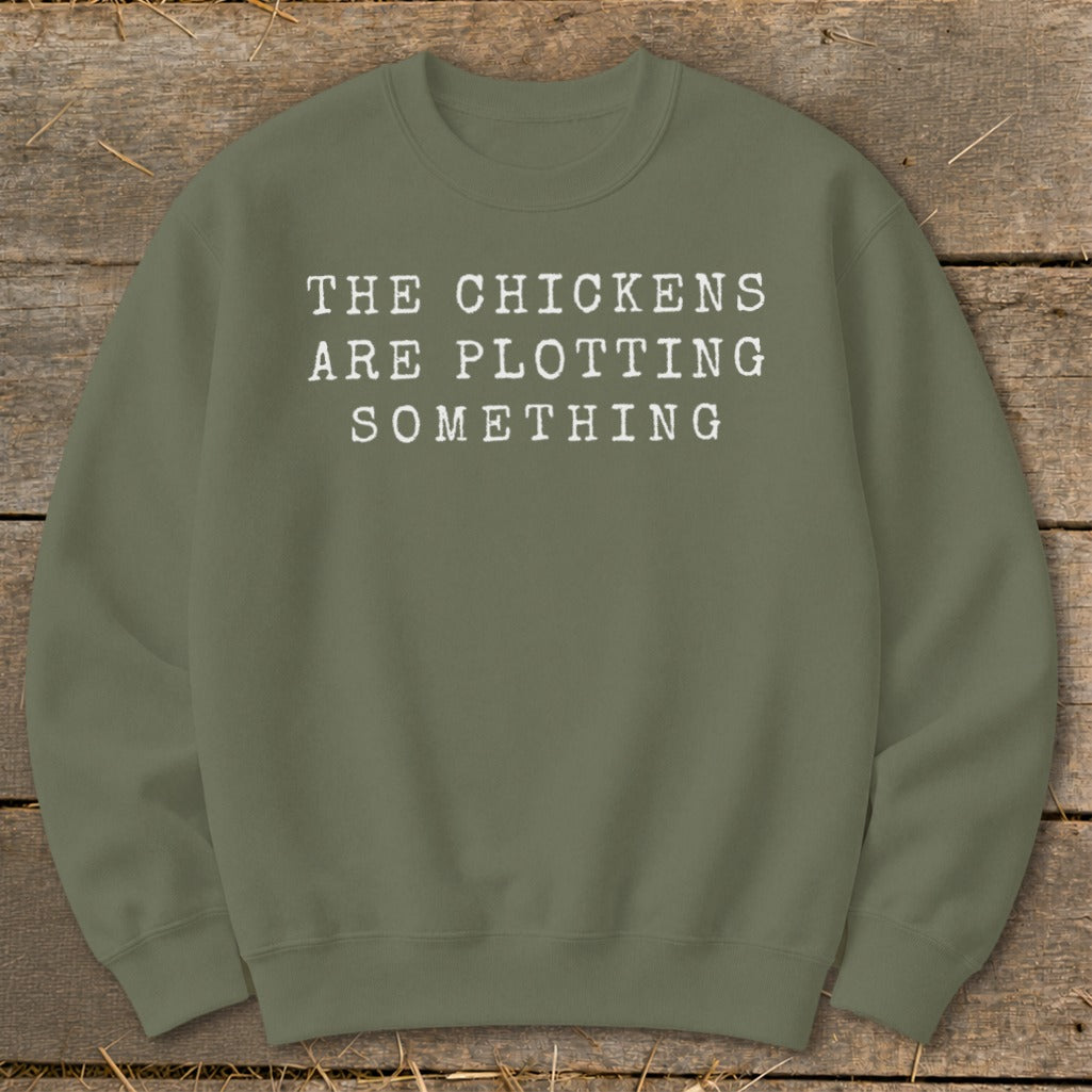 Olive green sweatshirt with white text reading "THE CHICKENS ARE PLOTTING SOMETHING."