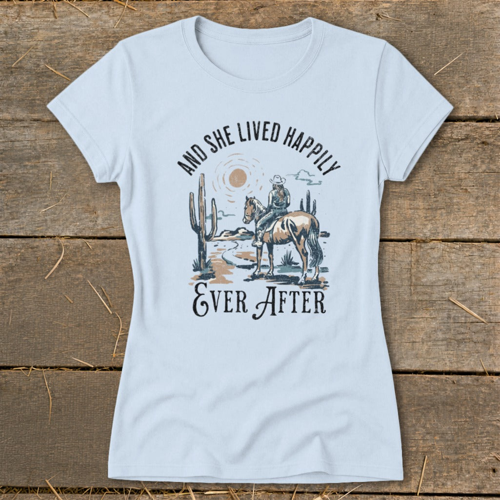 Light blue t-shirt with desert scene, horse rider, and text "AND SHE LIVED HAPPILY EVER AFTER."
