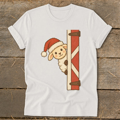 White t-shirt with a cartoon sheep wearing a Santa hat peeking from behind a red barn door.