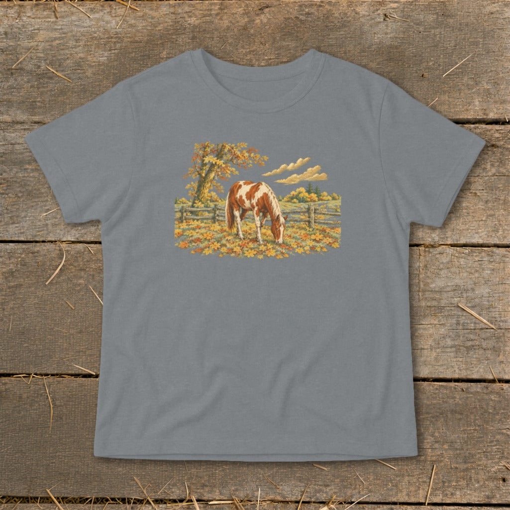 Brown and white horse grazing in a field of autumn leaves.