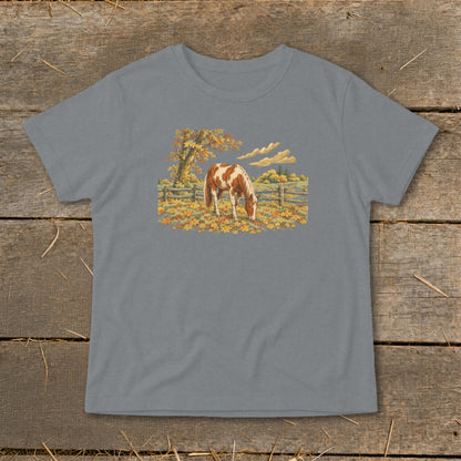 Brown and white horse grazing in a field of autumn leaves.