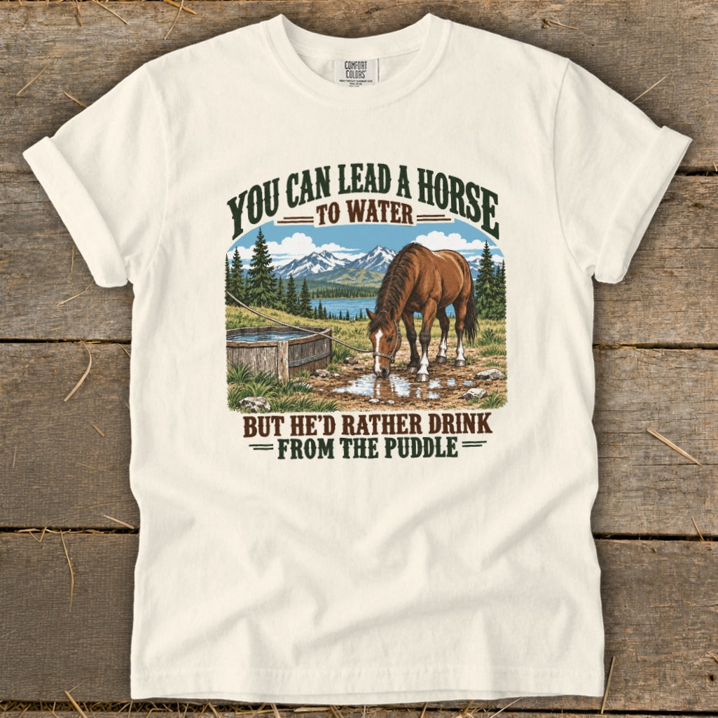 Cream-colored t-shirt with a vintage graphic of a horse drinking from a puddle and mountain scenery.