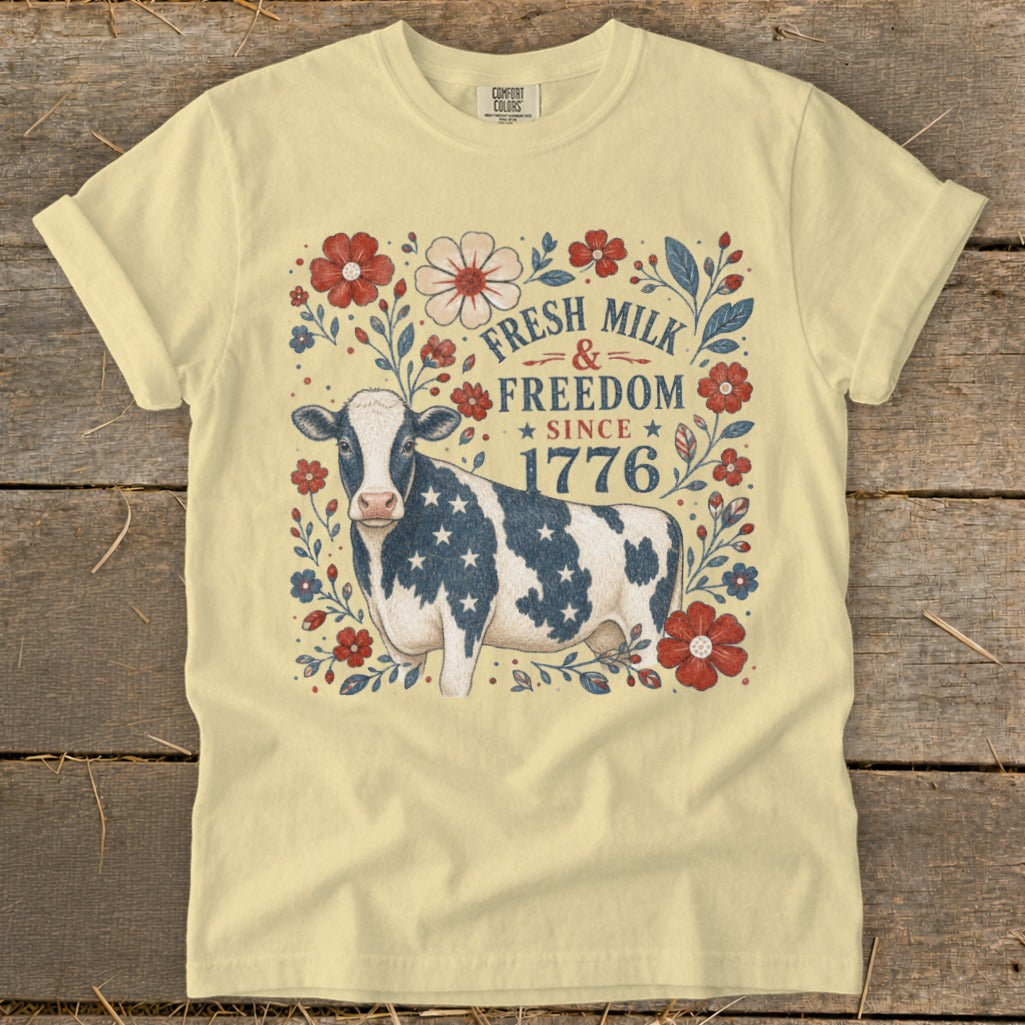 Cow with American flag pattern on shirt, surrounded by flowers and text "Fresh Milk & Freedom Since 1776".