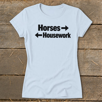 A light blue women's t-shirt printed with black text that reads Horses pointing right and Housework pointing left.