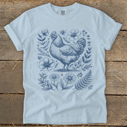 Light blue t-shirt with a blue line drawing of a chicken surrounded by flowers and foliage.