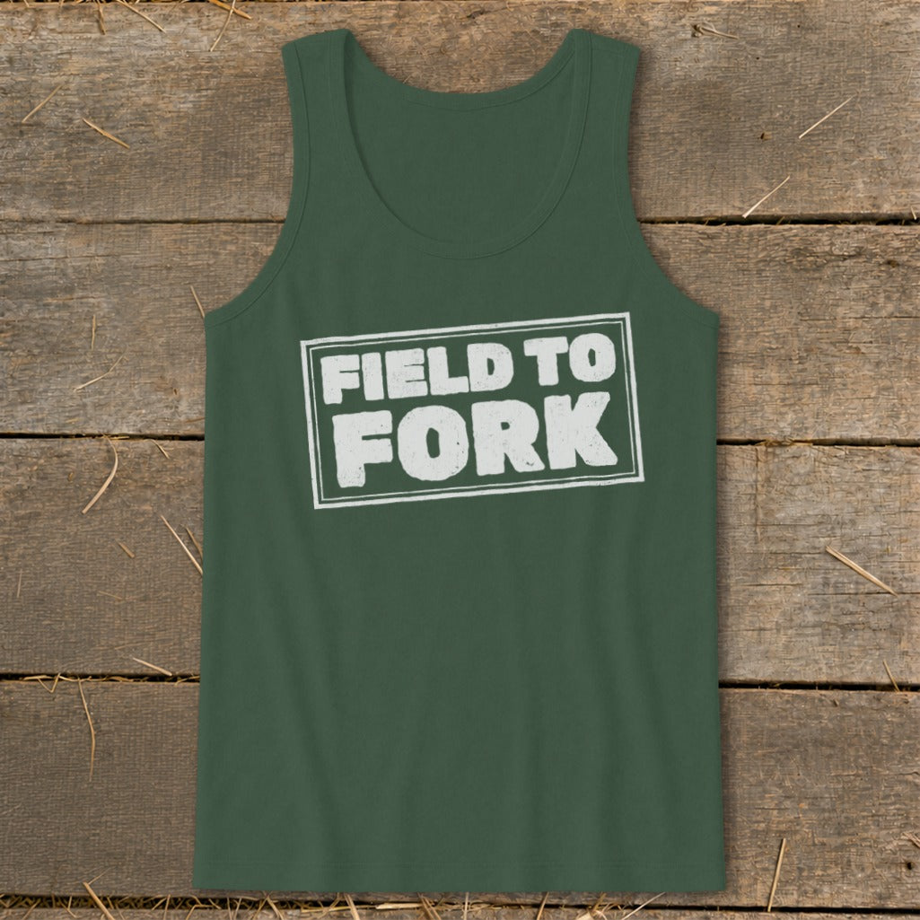 A dark green tank top featuring the white distressed text FIELD TO FORK centered on the chest, laid flat against a rustic wooden background.