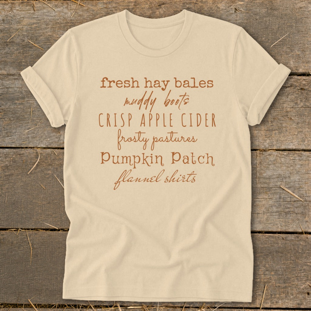 Cream t-shirt with text: fresh hay bales, muddy boots, crisp apple cider, frosty pastures, pumpkin patch, flannel shirts.
