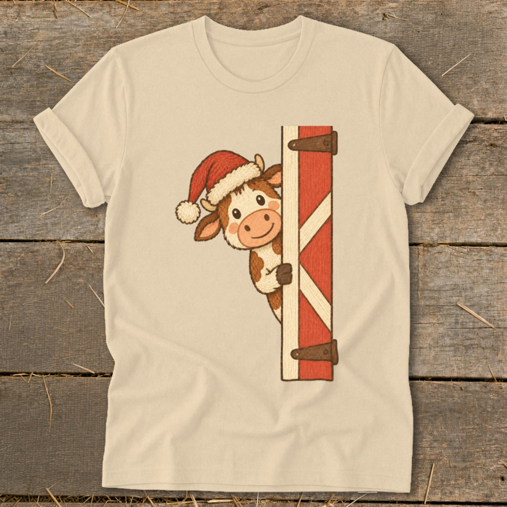 Cream t-shirt with a cartoon cow wearing a Santa hat peeking around a red barn door.
