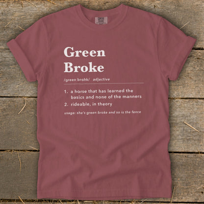 A mauve t-shirt with white text defining Green Broke laid flat on rustic wood.