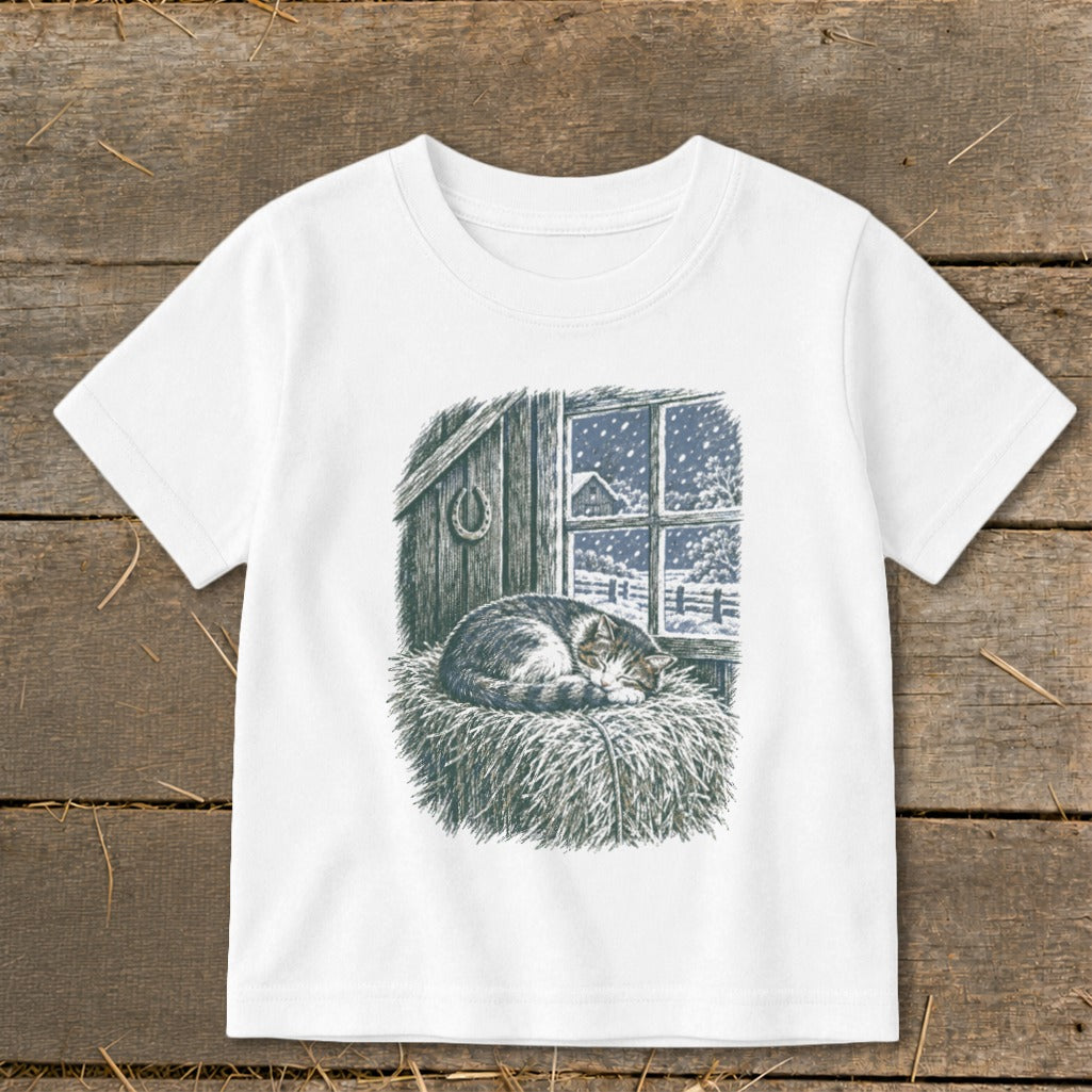 T-shirt with illustration of a sleeping cat on hay next to a snowy window.