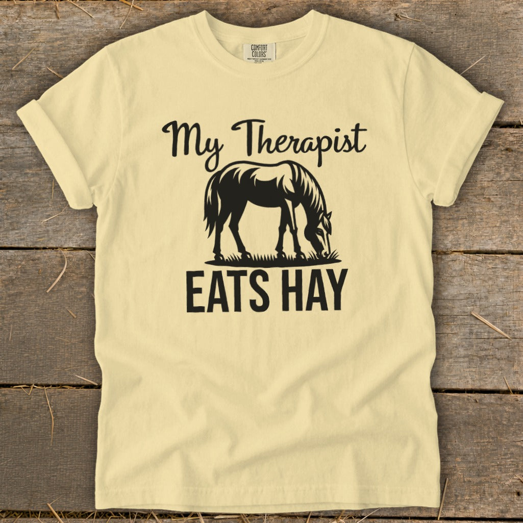 Light yellow t-shirt with black text "My Therapist Eats Hay" and horse graphic.