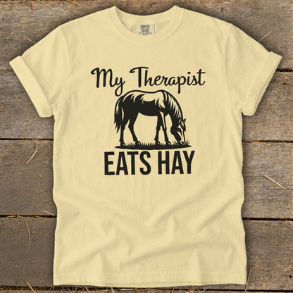 Light yellow t-shirt with black text "My Therapist Eats Hay" and horse graphic.