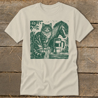 Linocut design of a cat, horse, mug, and barn on a cream t-shirt.