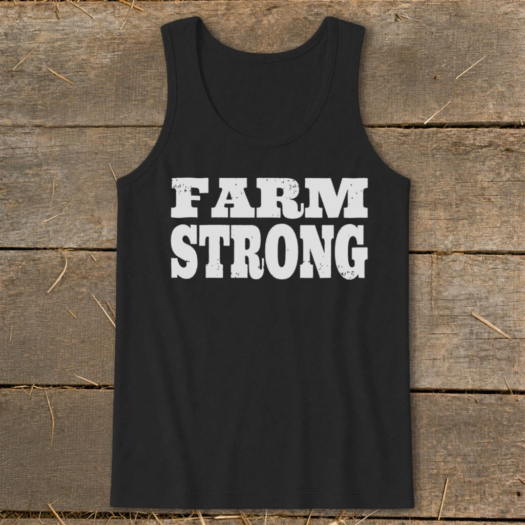 A black tank top with the distressed white text FARM STRONG laid flat on a rustic wooden background.