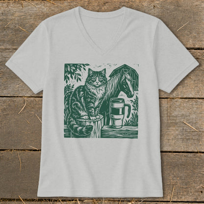 Green linocut print of cat, horse, barn, and mug on a light gray t-shirt.