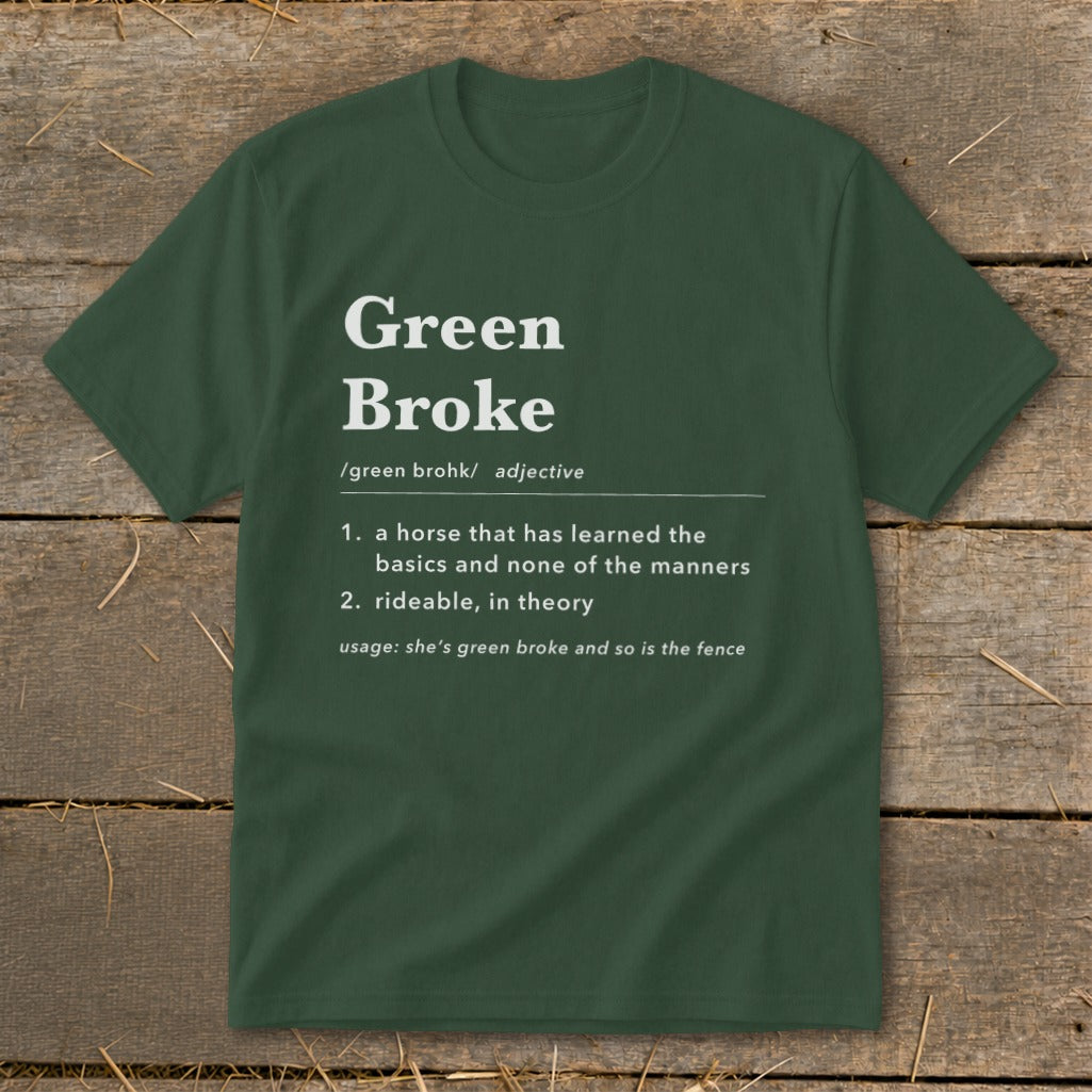 A dark green crewneck t-shirt featuring dictionary-style text that defines green broke on a rustic wooden background.