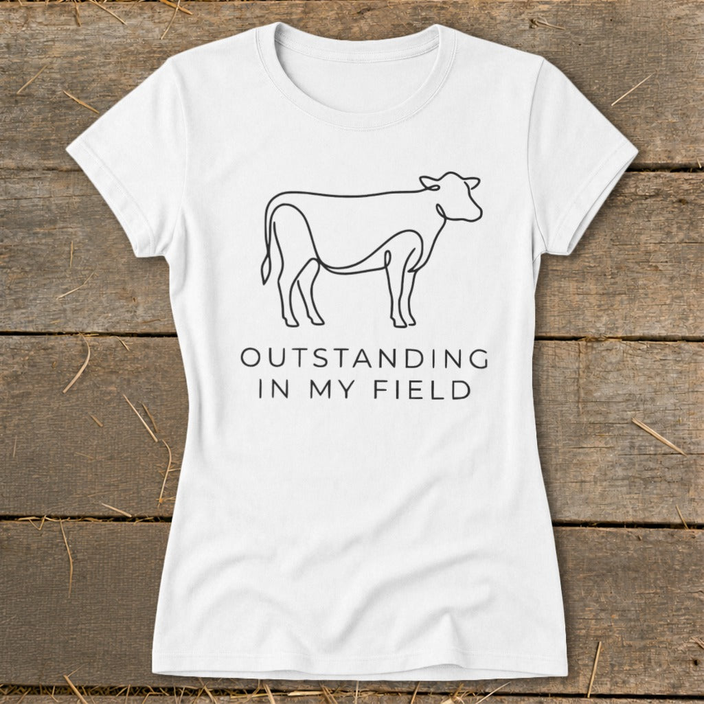 White t-shirt with line art of a cow and text "OUTSTANDING IN MY FIELD".