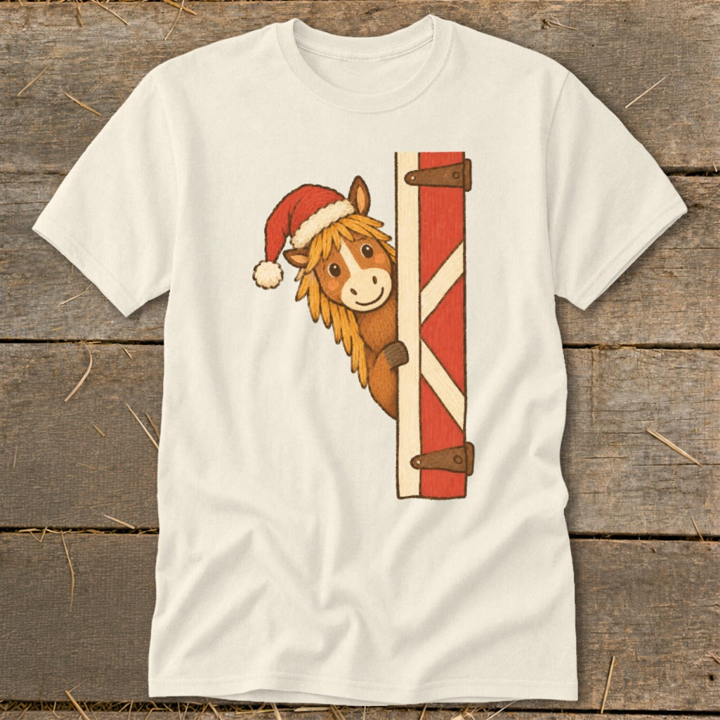 Cream t-shirt with a cartoon horse wearing a Santa hat peeking around a red barn door.