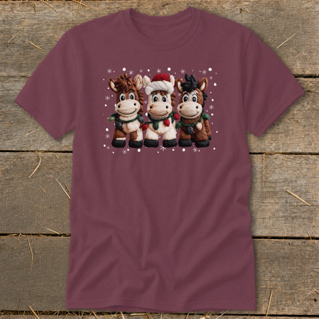 Three cartoon horses wearing holiday lights and a Santa hat on a burgundy shirt.