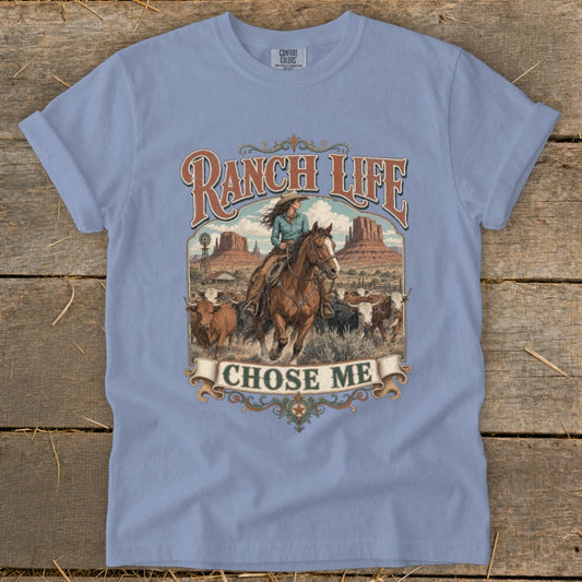 Ranch Life Chose Me graphic with cowgirl on horseback and cattle on a light blue t-shirt.
