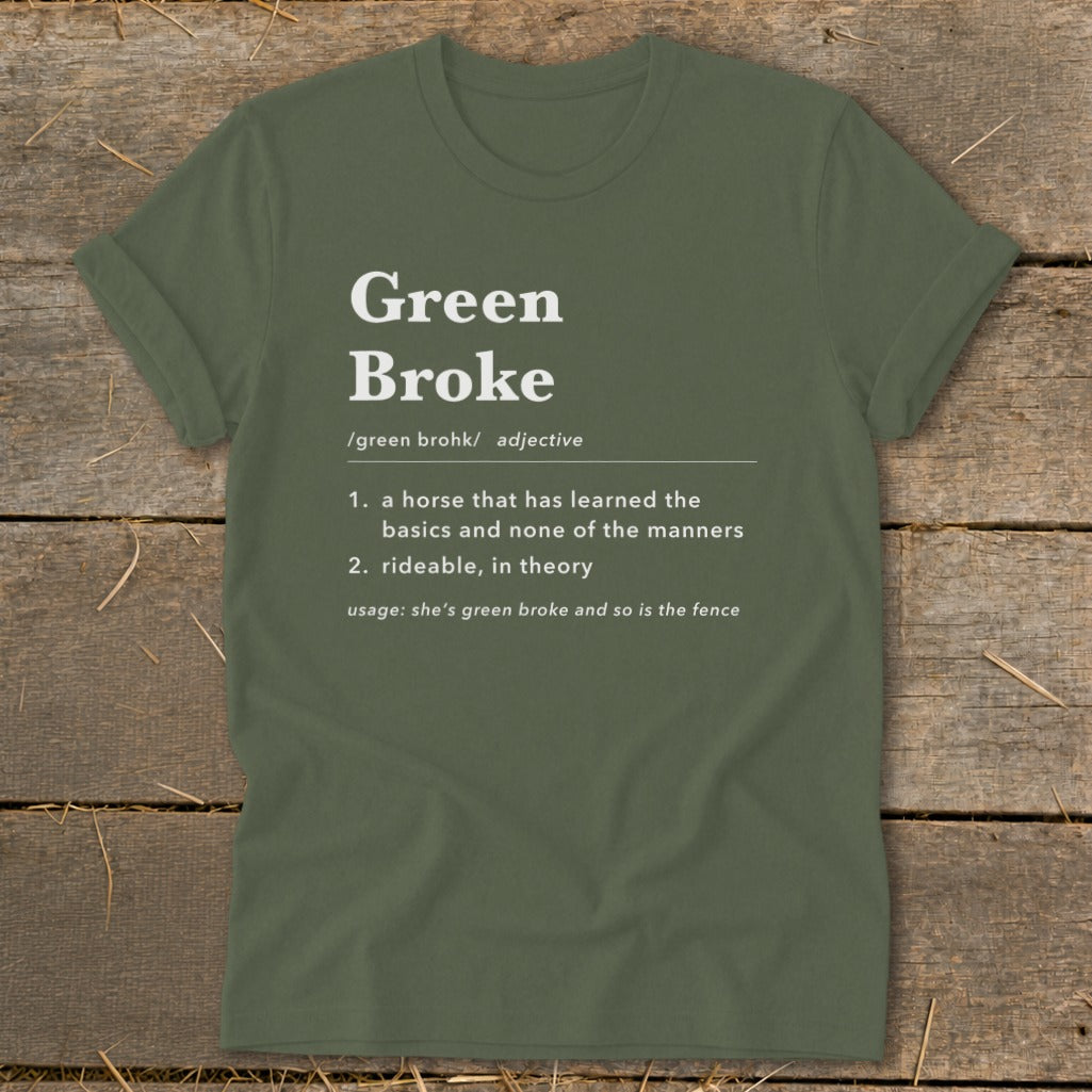 Olive green t-shirt with white text defining Green Broke laid flat on wooden boards.
