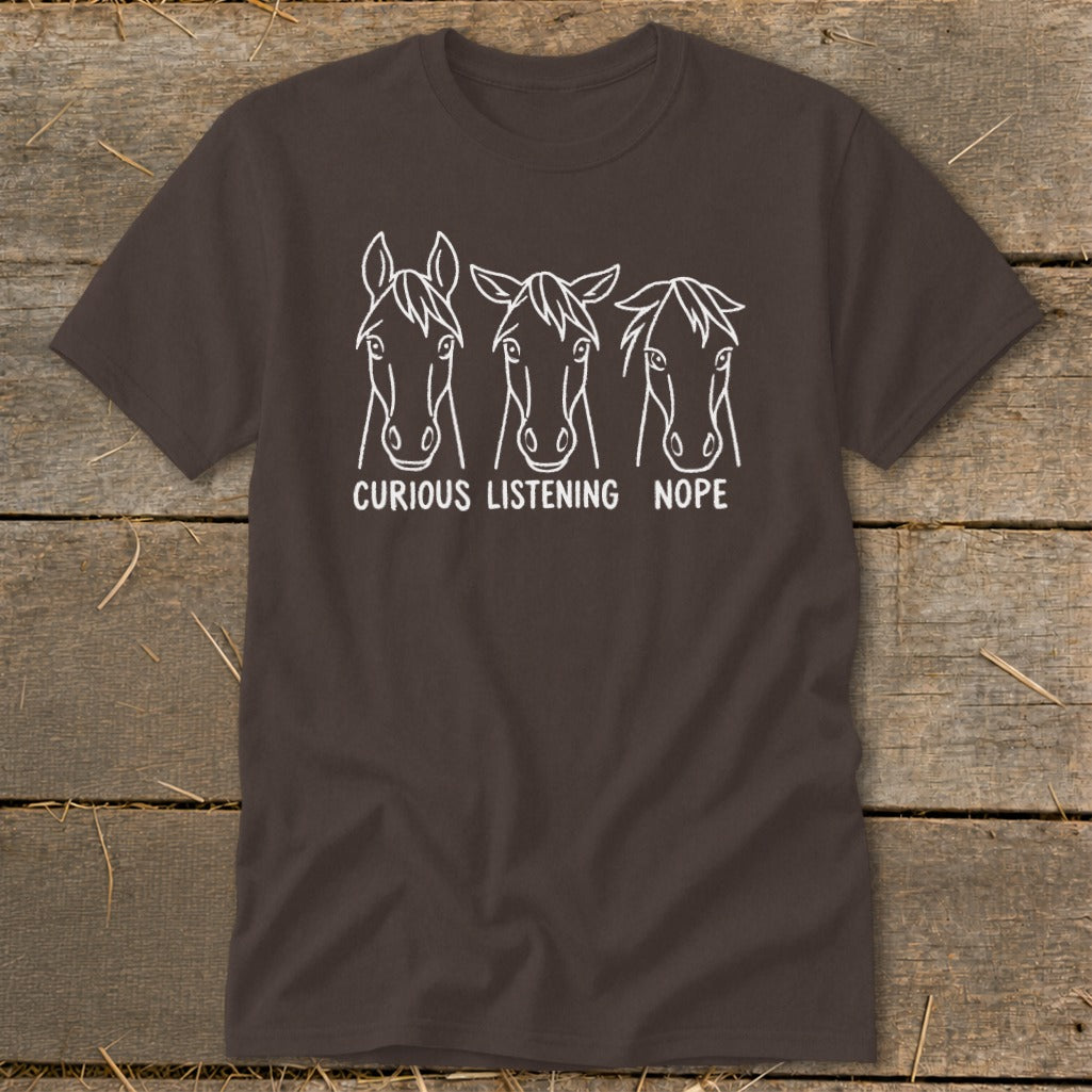 A dark brown t-shirt featuring three horse head illustrations with the text CURIOUS LISTENING NOPE below them.