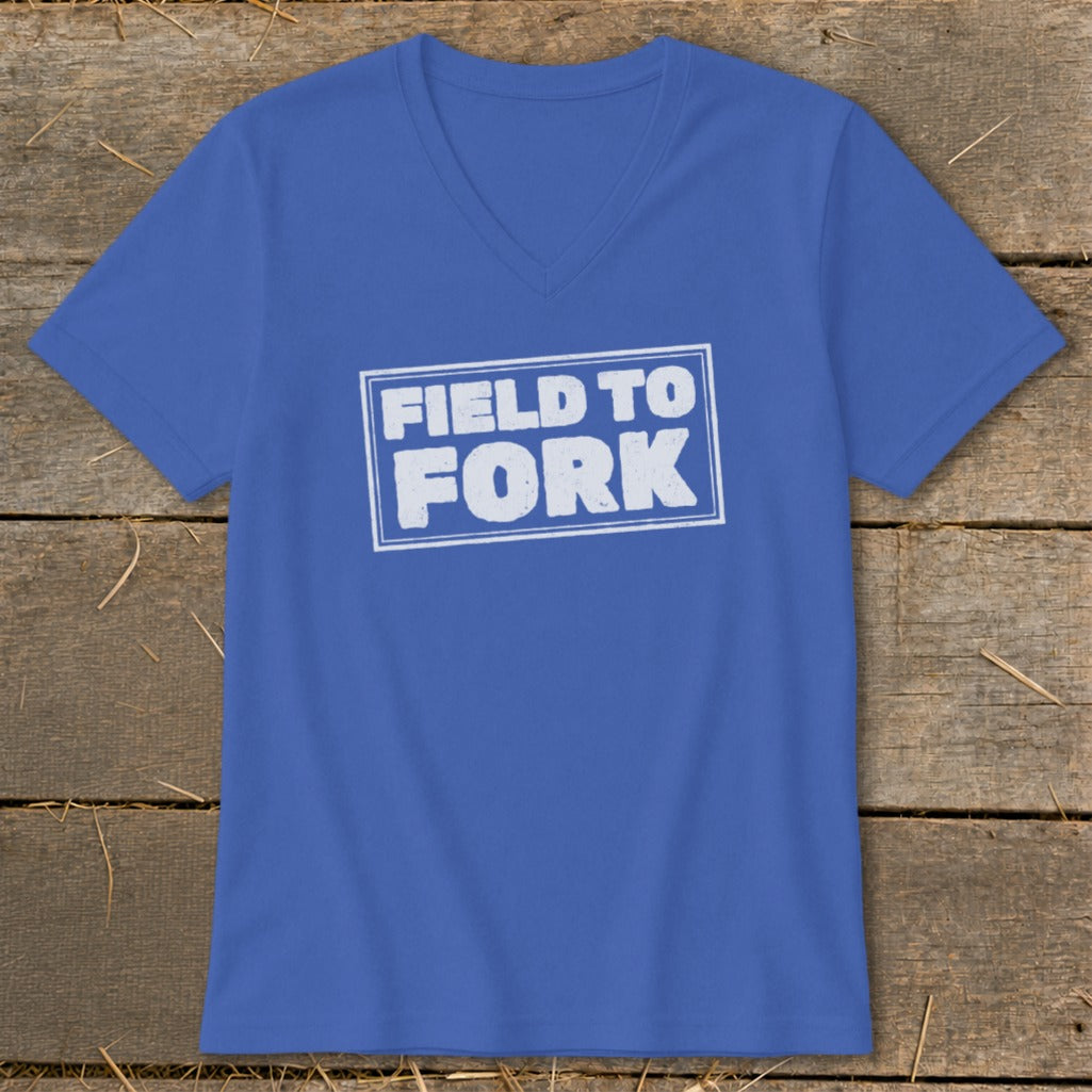 A blue V-neck t-shirt with white text that reads FIELD TO FORK centered on a wooden background.
