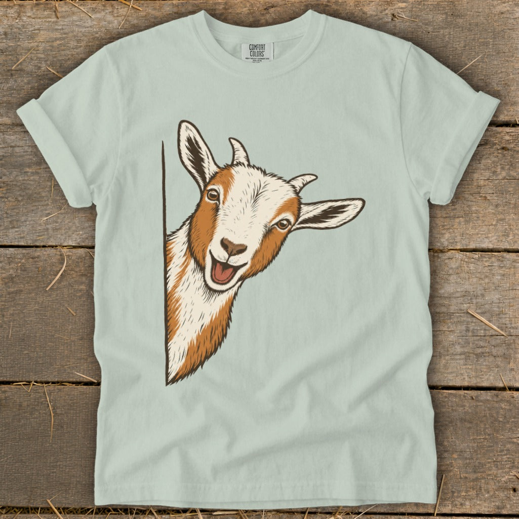 Illustration of a happy goat peeking from behind a corner on a light blue t-shirt.