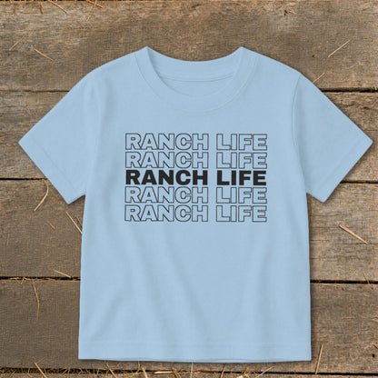 Light blue short-sleeved children's t-shirt printed with the text Ranch Life on a rustic wooden background.