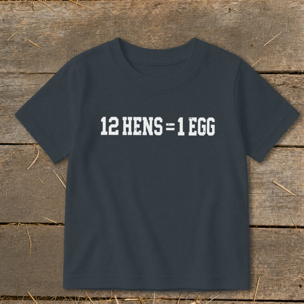 A dark grey t-shirt with distressed white text reading 12 HENS = 1 EGG, laid flat on a rustic wooden background.