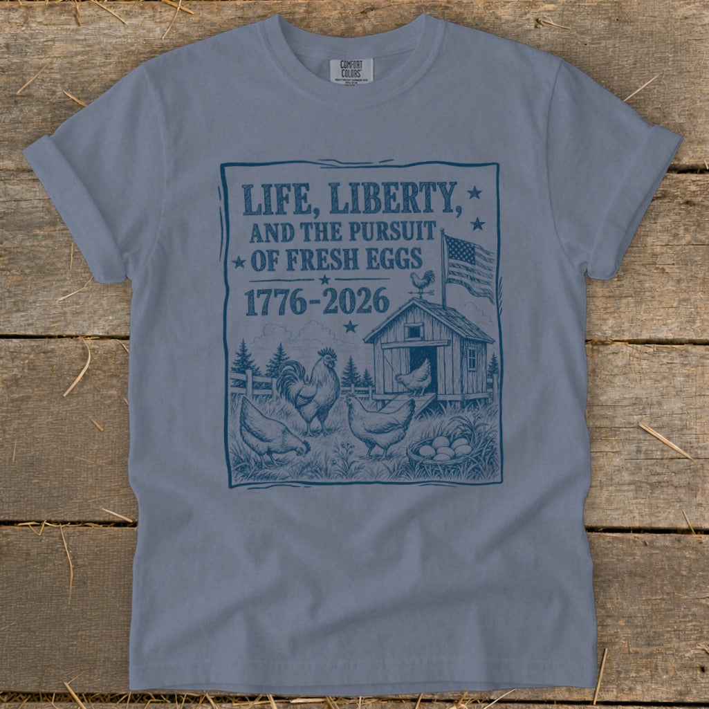 Blue t-shirt with "Life, Liberty, and the Pursuit of Fresh Eggs 1776-2026" graphic.