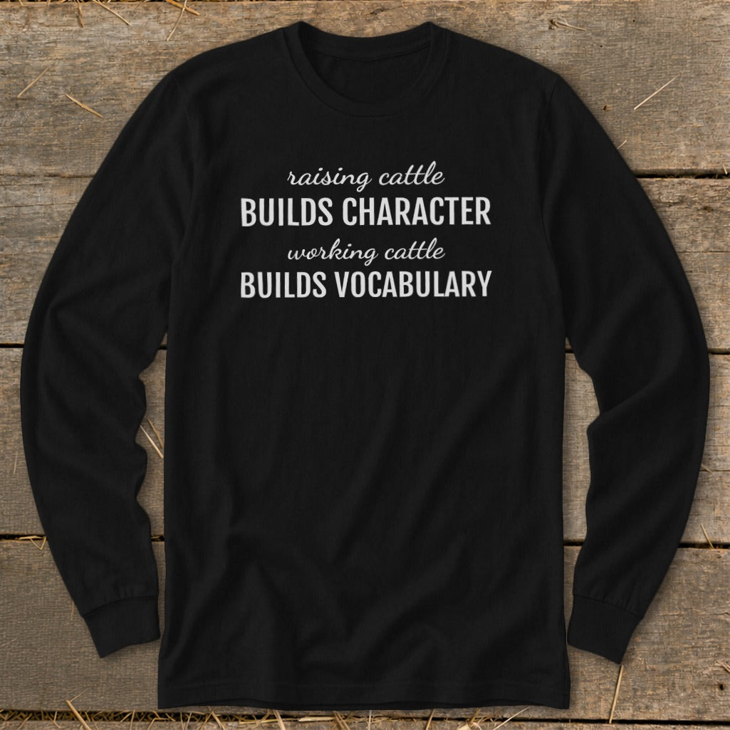 Black long sleeve shirt with white text reading "raising cattle BUILDS CHARACTER working cattle BUILDS VOCABULARY".