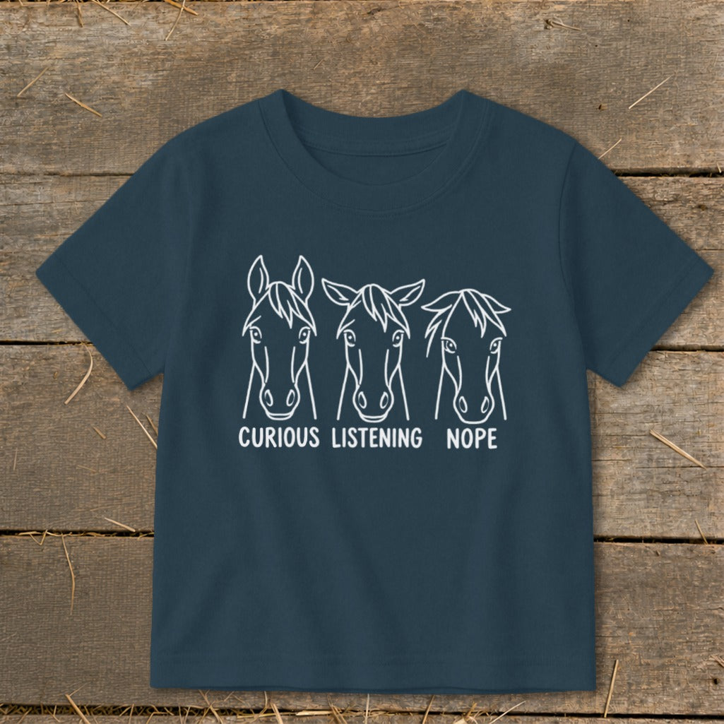 Dark blue short-sleeved children's t-shirt featuring a white graphic of three horse heads with the captions Curious, Listening, and Nope.