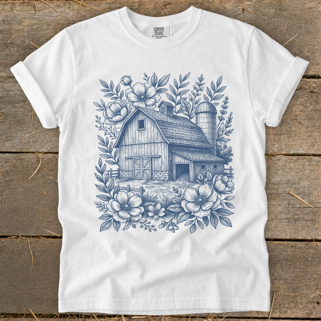 White t-shirt with a blue sketch of a barn, silo, fence, and floral border.