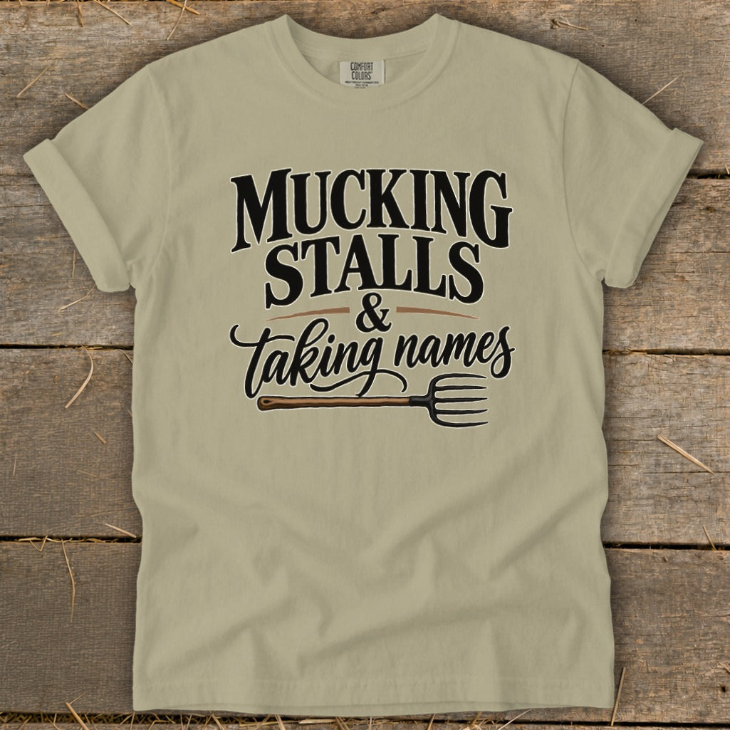 Tan t-shirt with "Mucking Stalls & Taking Names" text and pitchfork graphic.