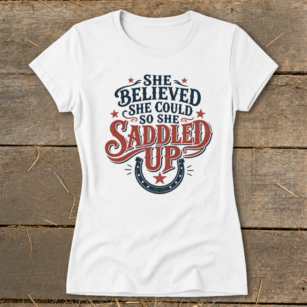 White t-shirt with "She believed she could so she saddled up" graphic.