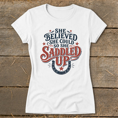White t-shirt with "She believed she could so she saddled up" graphic.