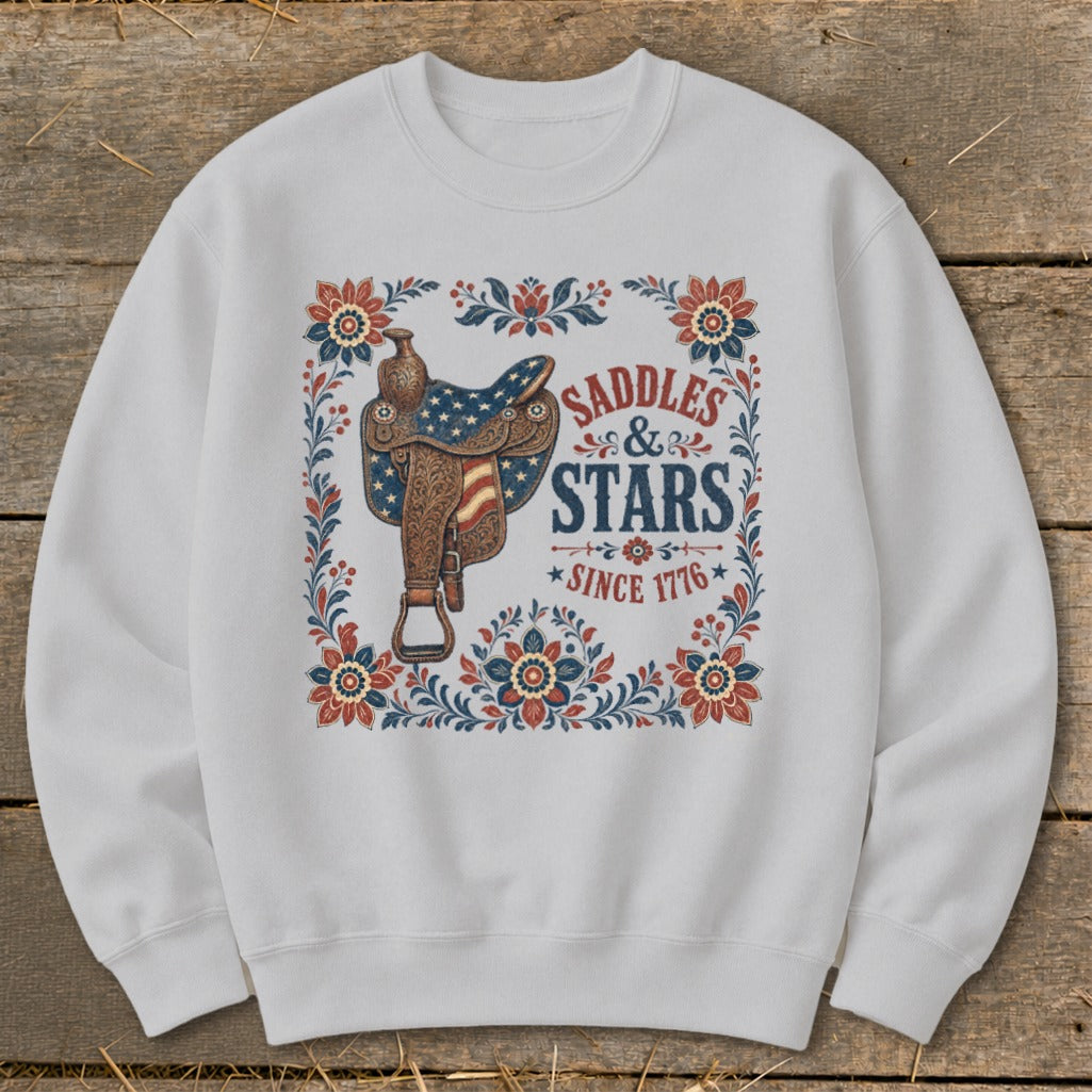 White sweatshirt with "Saddles & Stars Since 1776" text and American flag saddle graphic.