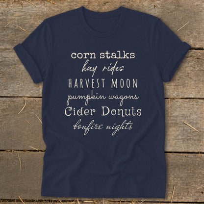 Navy t-shirt with "corn stalks hay rides HARVEST MOON pumpkin wagons Cider Donuts bonfire nights" text.