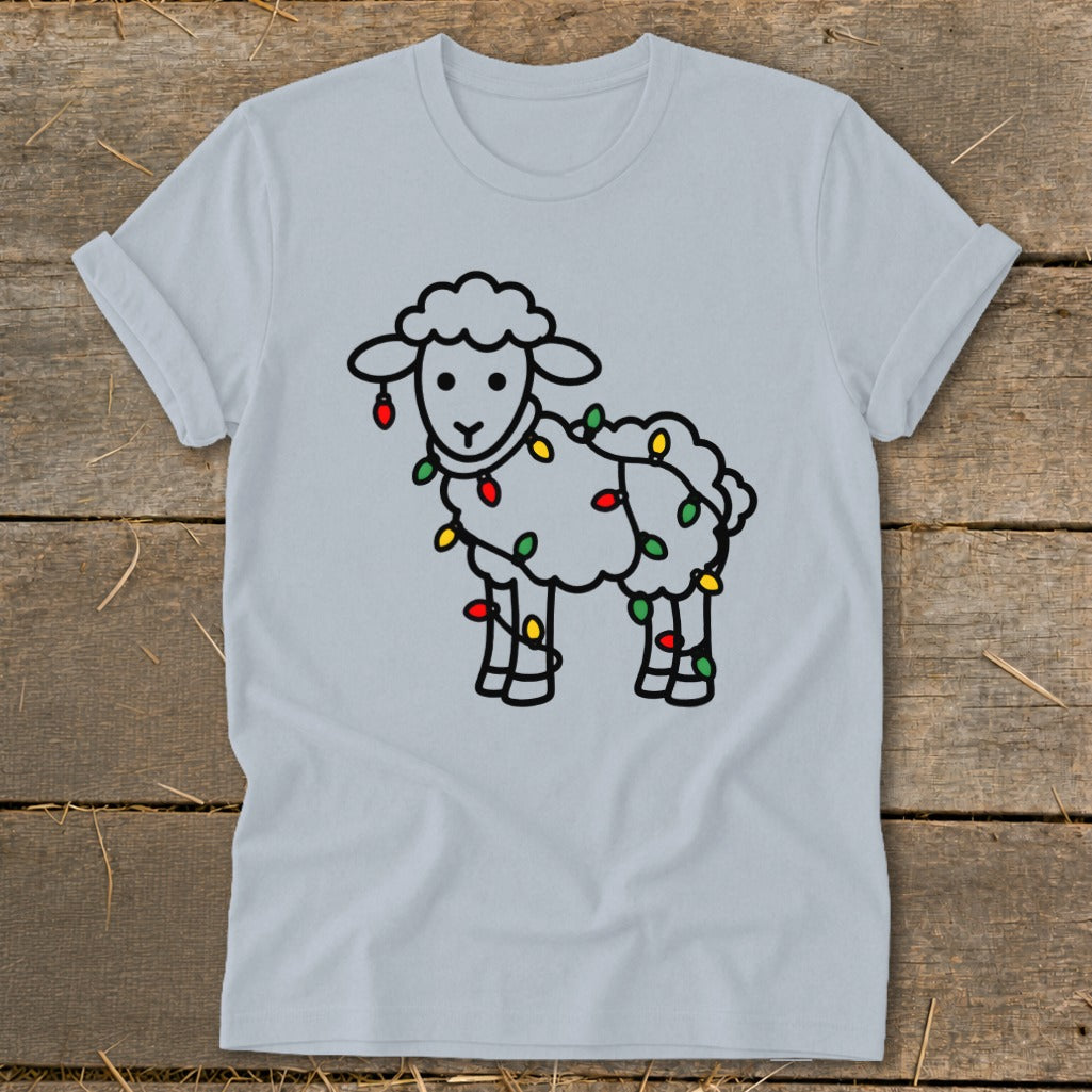 Light blue t-shirt featuring a cartoon sheep tangled in colorful Christmas lights, displayed on a wooden background.