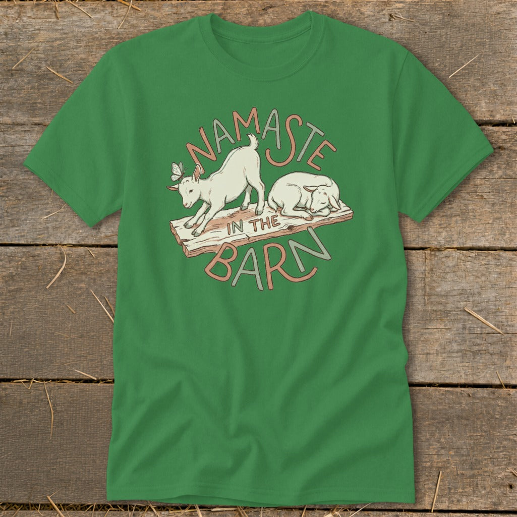Green t-shirt with "Namaste in the Barn" text and cartoon goats on a wooden plank.