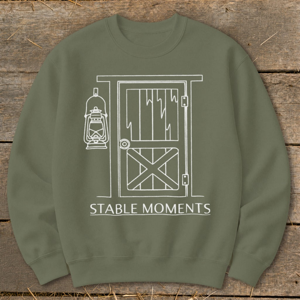 Olive green sweatshirt with white line drawing of a barn door and lantern with text "STABLE MOMENTS".