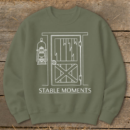 Olive green sweatshirt with white line drawing of a barn door and lantern with text "STABLE MOMENTS".