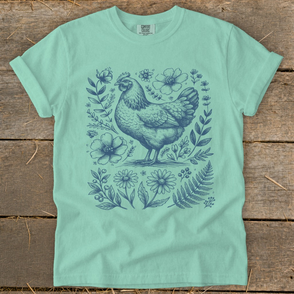 Mint t-shirt with a blue line drawing of a hen surrounded by flowers and leaves.