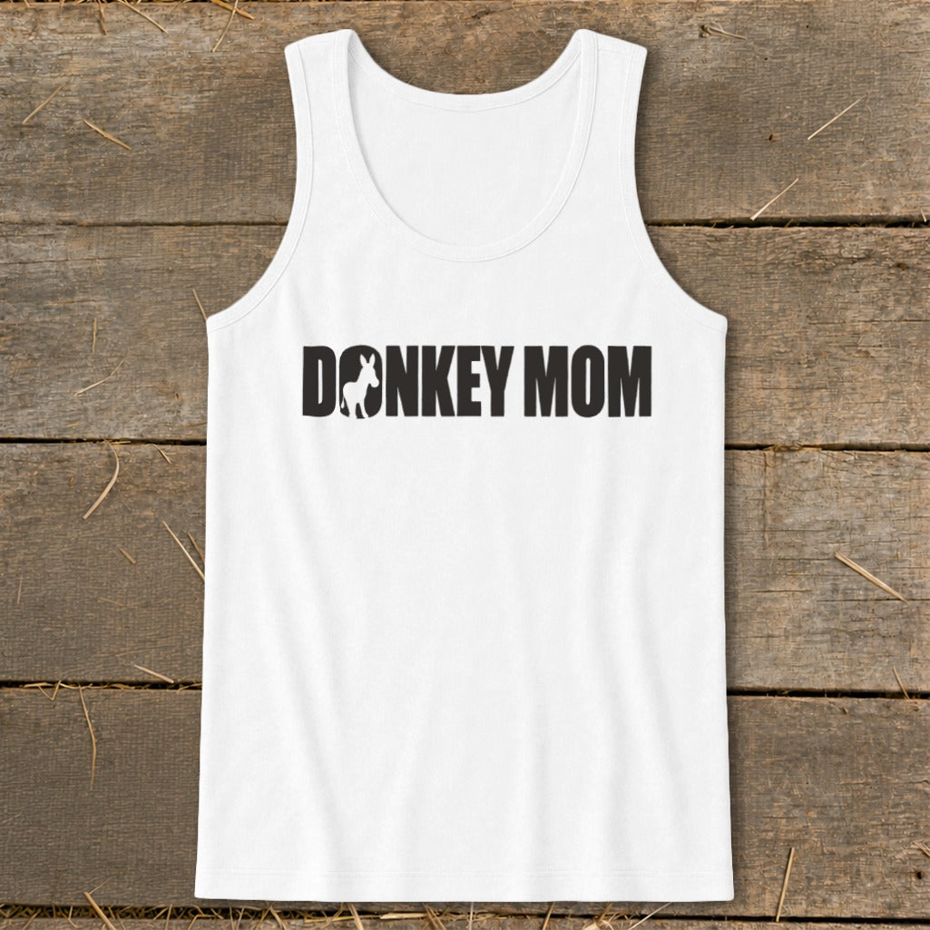 White women's tank top featuring the black text Donkey Mom with a donkey silhouette inside the letter O, displayed on a wooden surface.