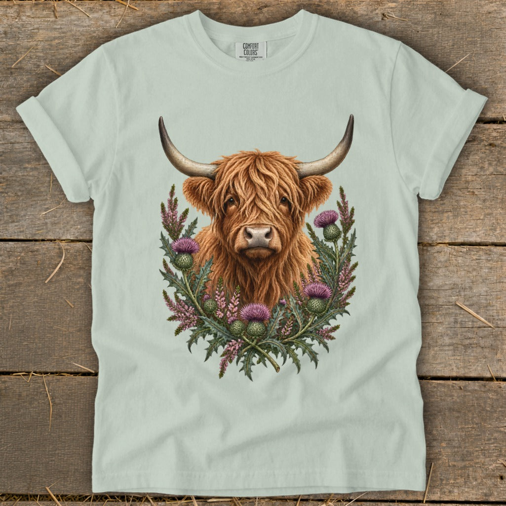 Highland cow portrait surrounded by thistles on a light green t-shirt.