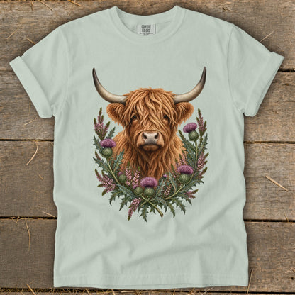 Highland cow portrait surrounded by thistles on a light green t-shirt.