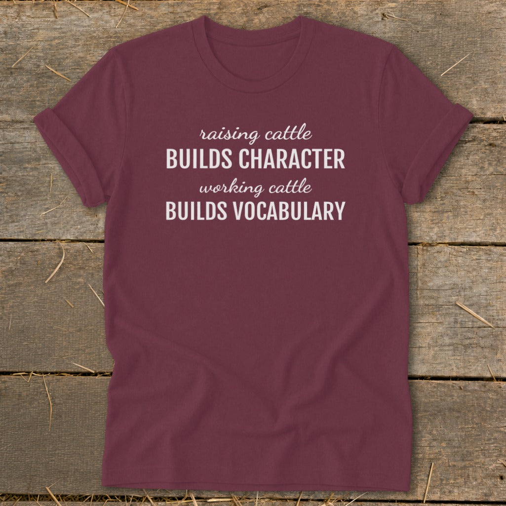 Maroon t-shirt with white text: "raising cattle BUILDS CHARACTER, working cattle BUILDS VOCABULARY"